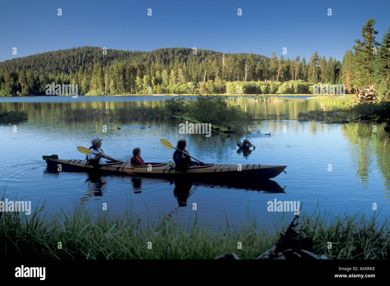 Family paddles homemade wooden kayak on blue water at Manzanita Lake Lassen Volcanic National