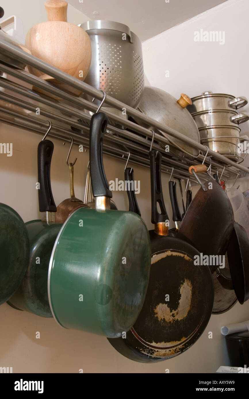 Clutter of pans and cooking utensils hanging from stainless steel shelf ...