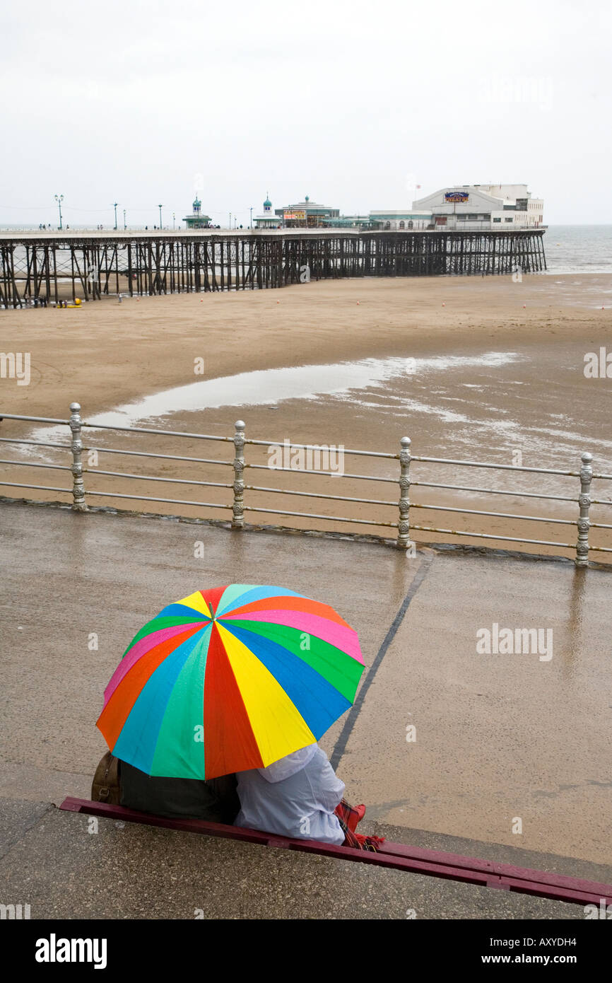 Couple sheltering from the rain on Blackpool promenade with view to the ...