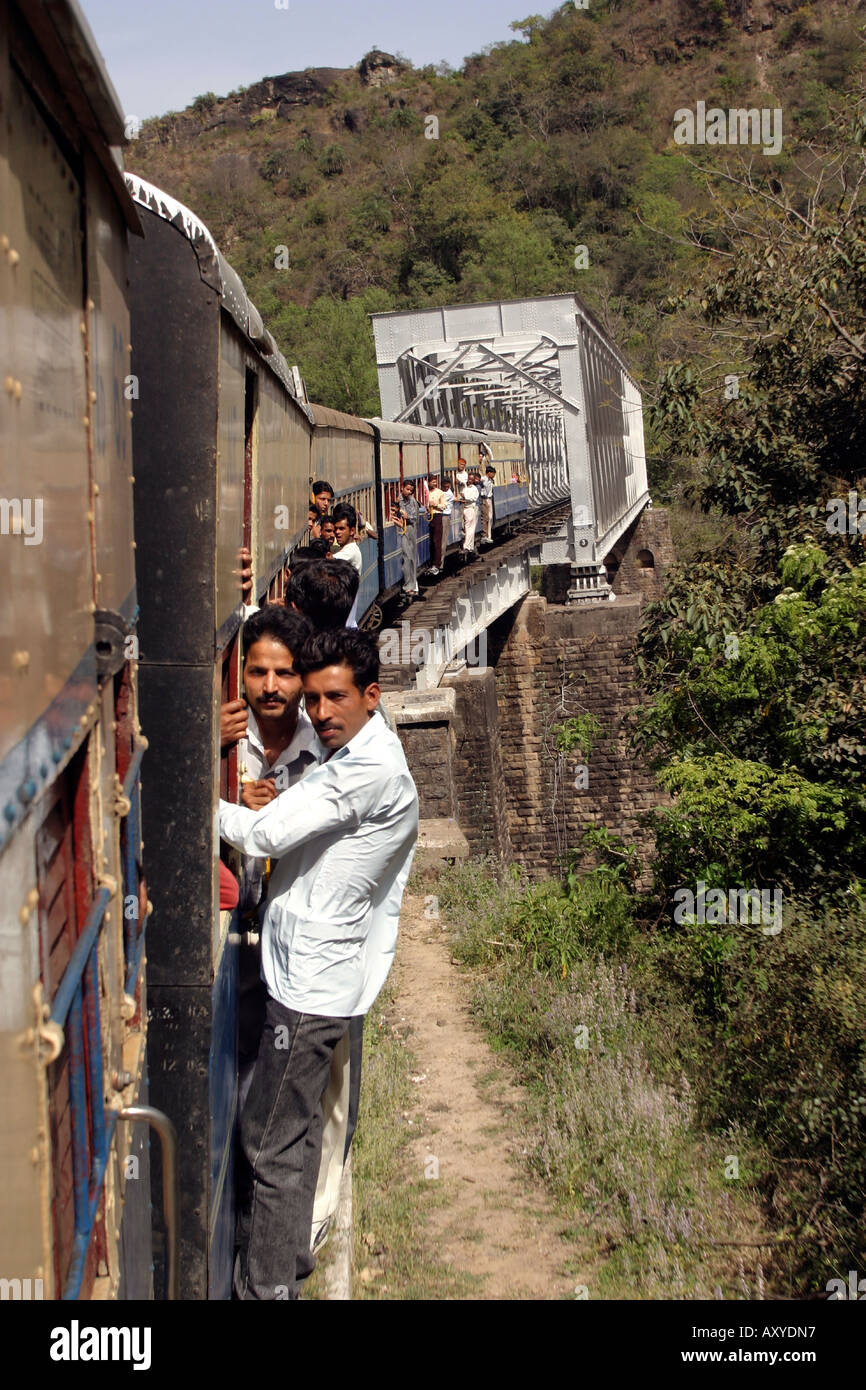 India Himachal Pradesh transport passengers hanging onto outside of rural narrow gauge train crossing a river bridge Stock Photo