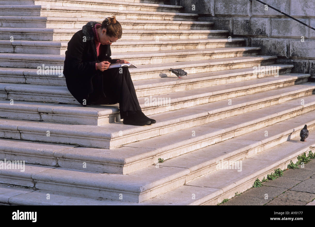 Woman Reading A Guide woman dressed in a dark coat reading a guide book on the steps of the ...