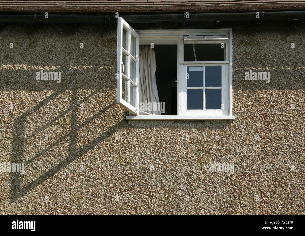 Open window of a house casting a strong geometric shadow across pebble dash wall Stock Photo