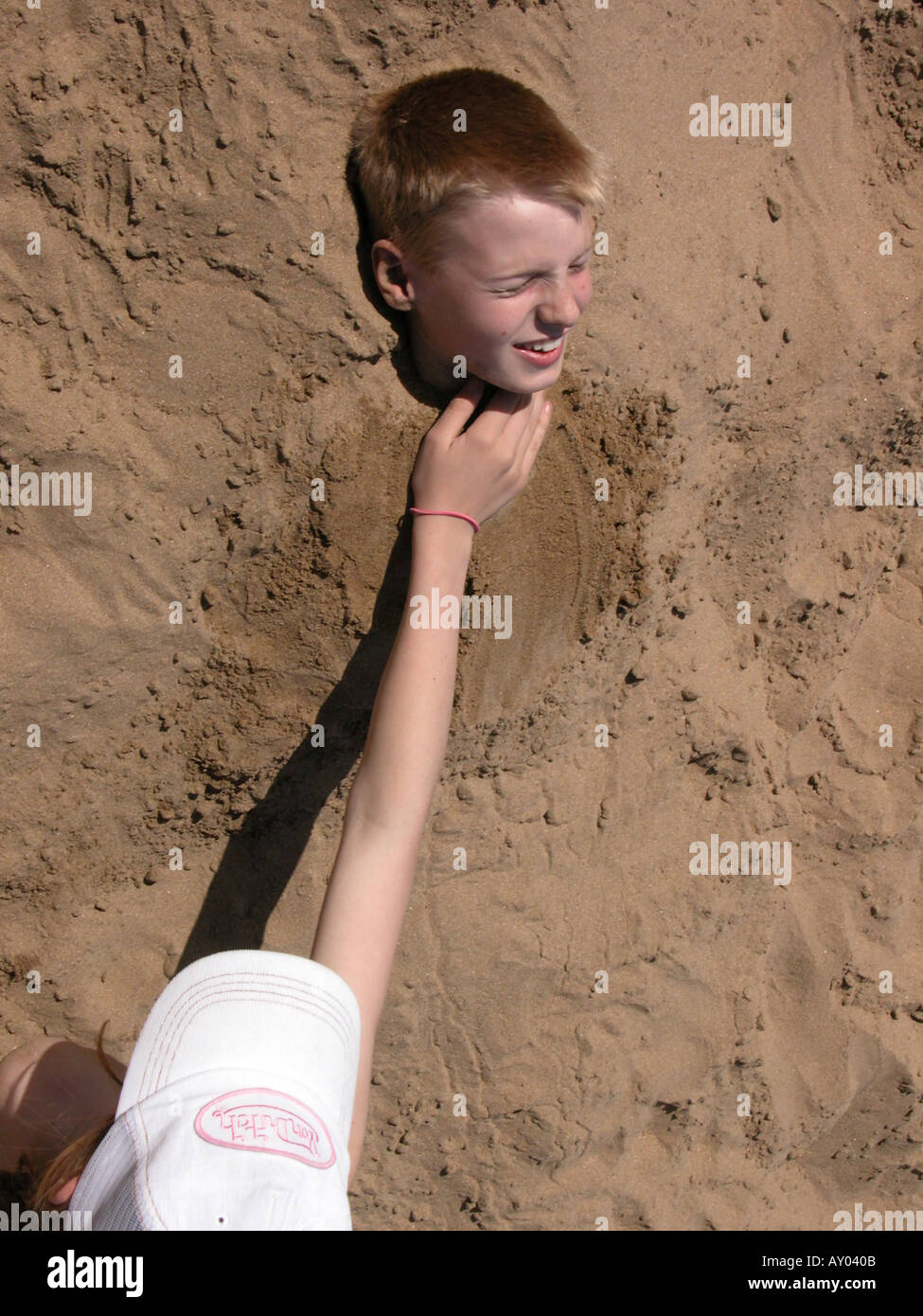 a boy being buried in the sand by a girl with only head showing Stock
