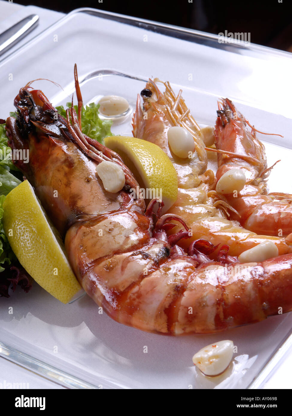 Three different sizes of gamba on a glass plate with lemon and garlic Stock Photo