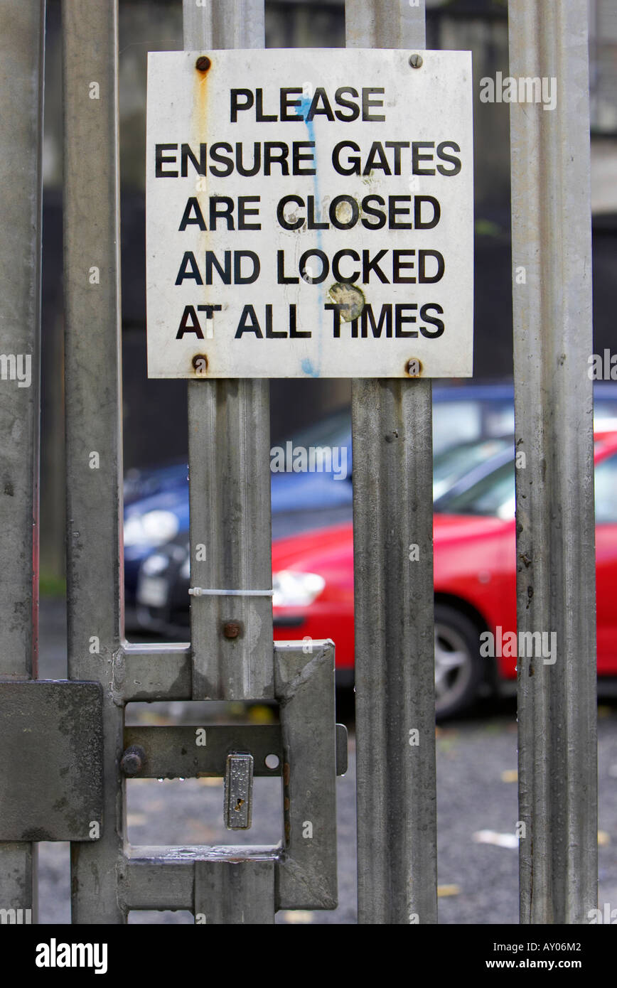 padlock locking metal gate car park entrance with please ensure gates are closed and locked Stock Photo