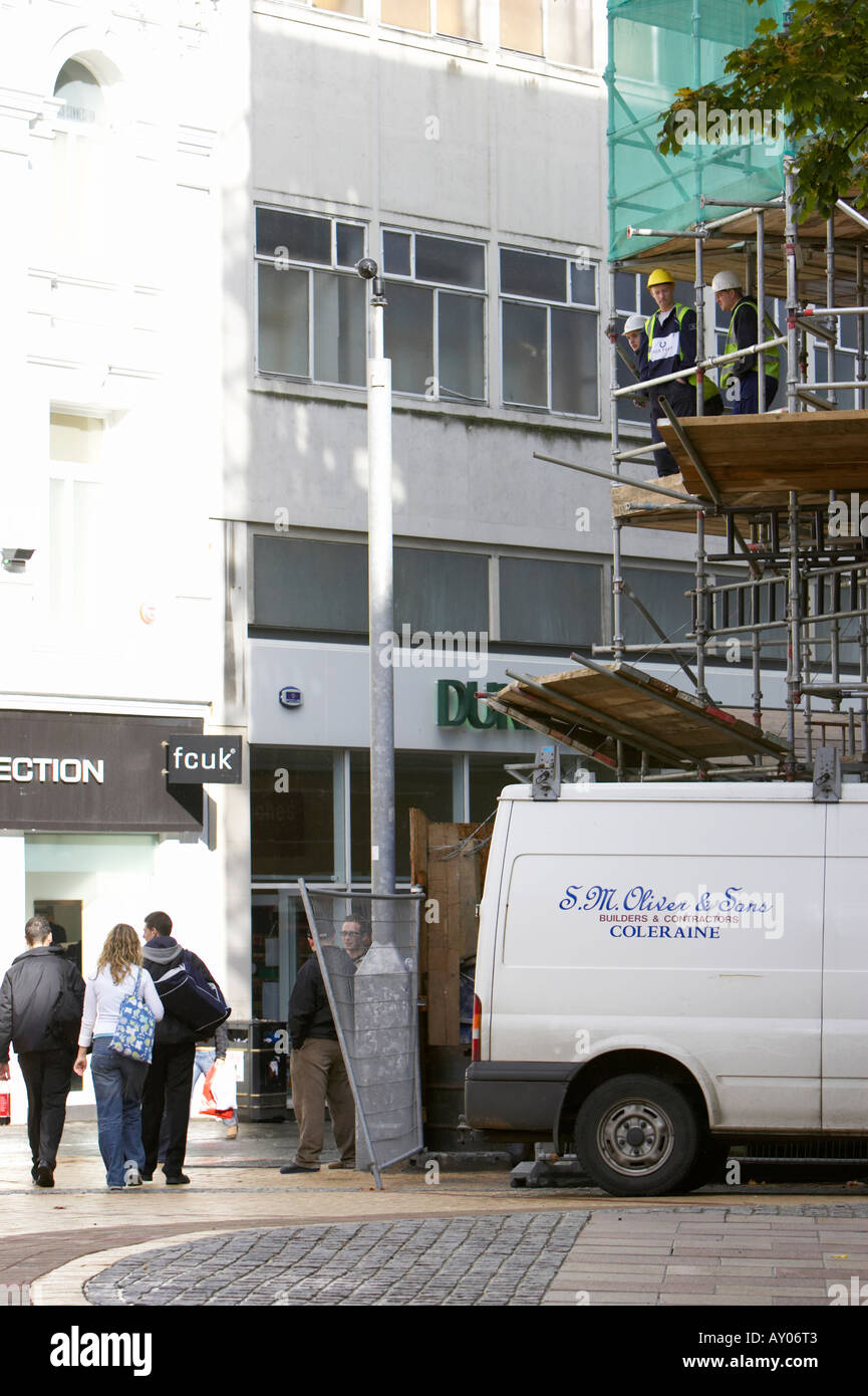 builders on scaffolding looking down at passing pedestrians in Belfast City Centre Stock Photo