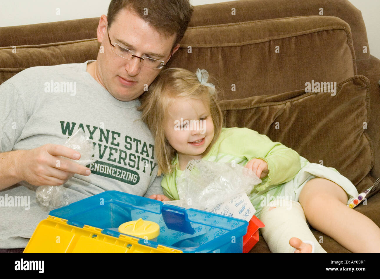 Little girl with broken leg reviews contents of a new toy box Stock Photo