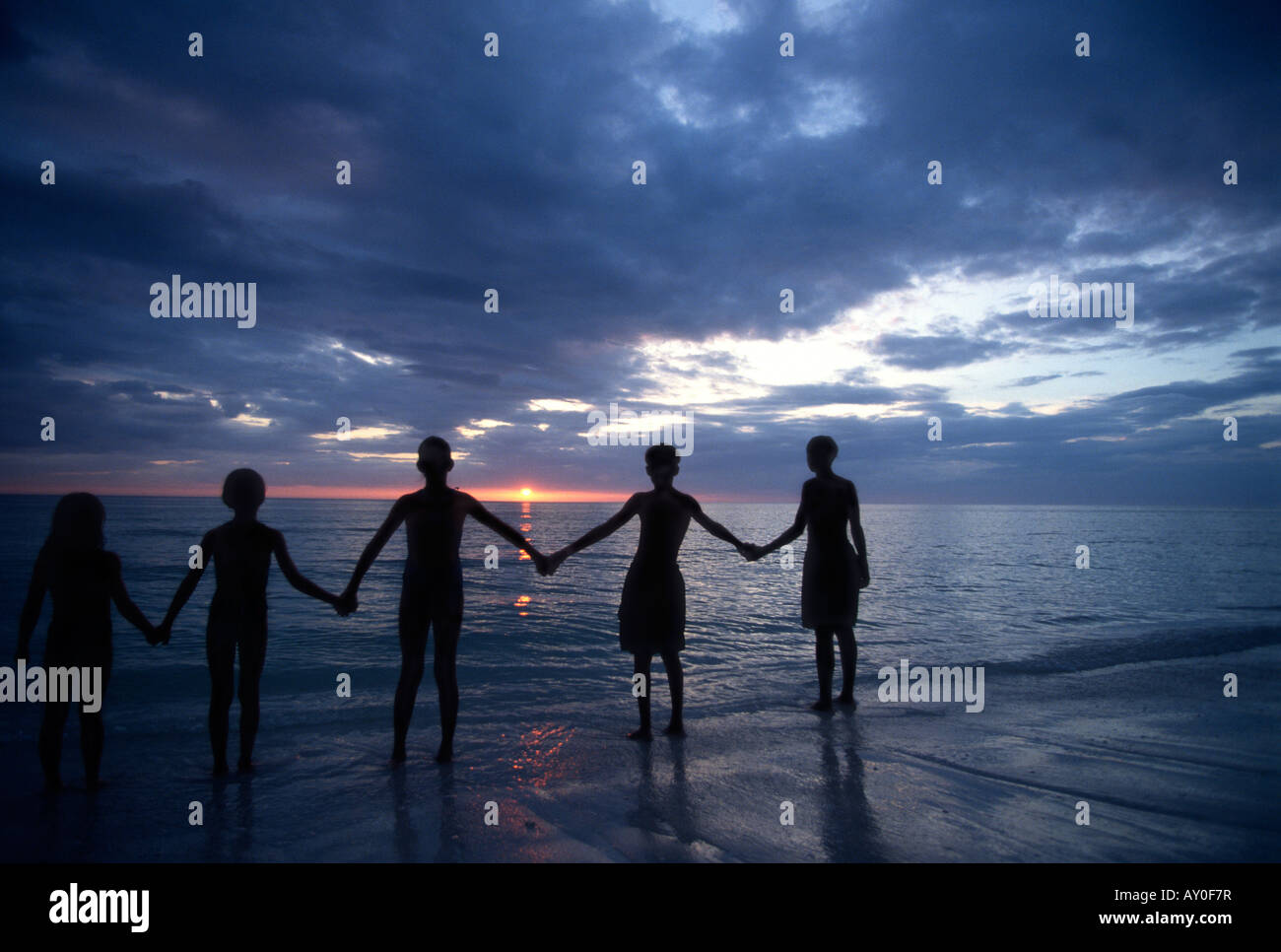 Children with outstretched arms holding hands at sunset silhouette Stock Photo