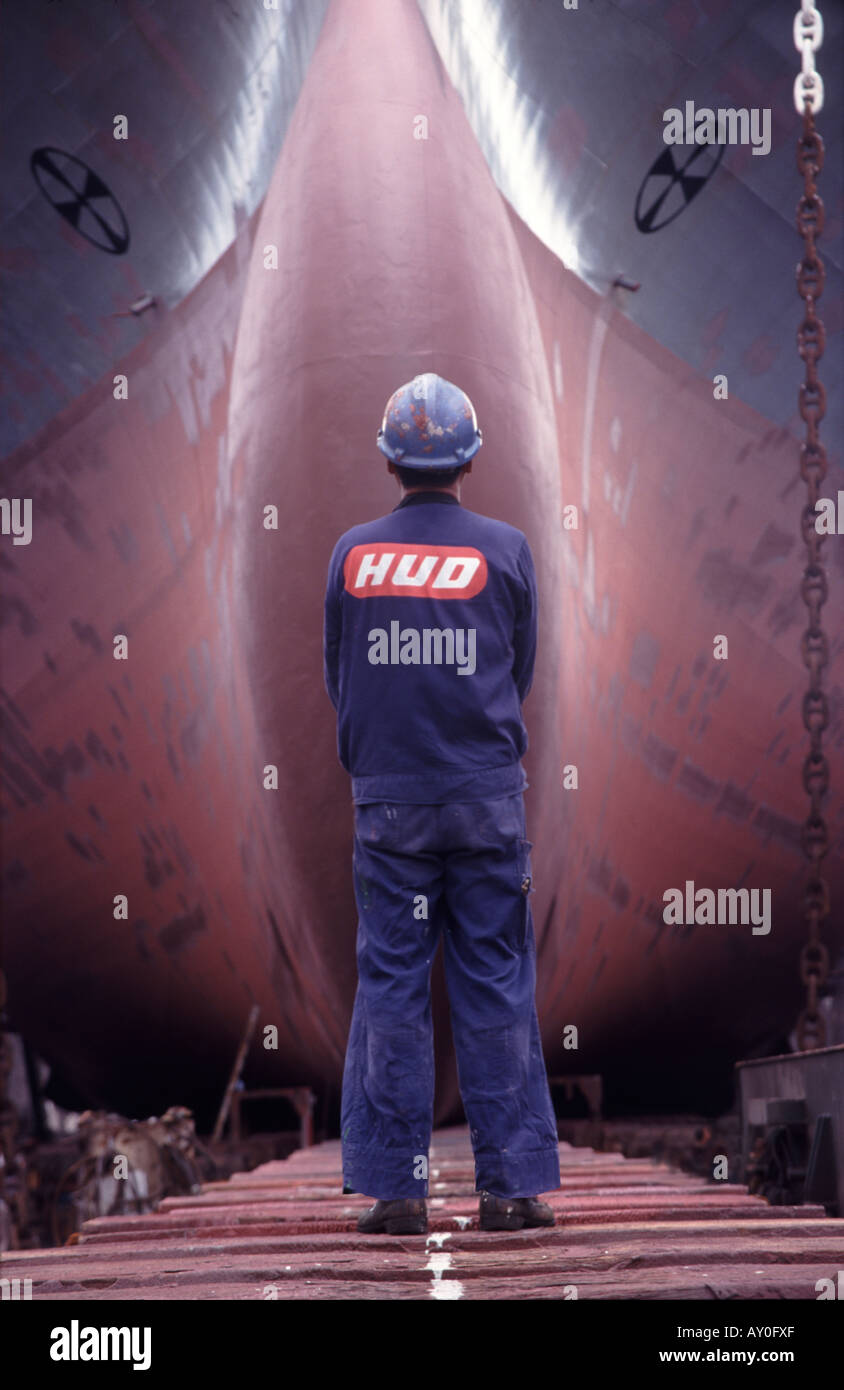 shipworker standing in front of the bow of a huge containership in drydock at hong long united dockyard fareast asia sar Stock Photo