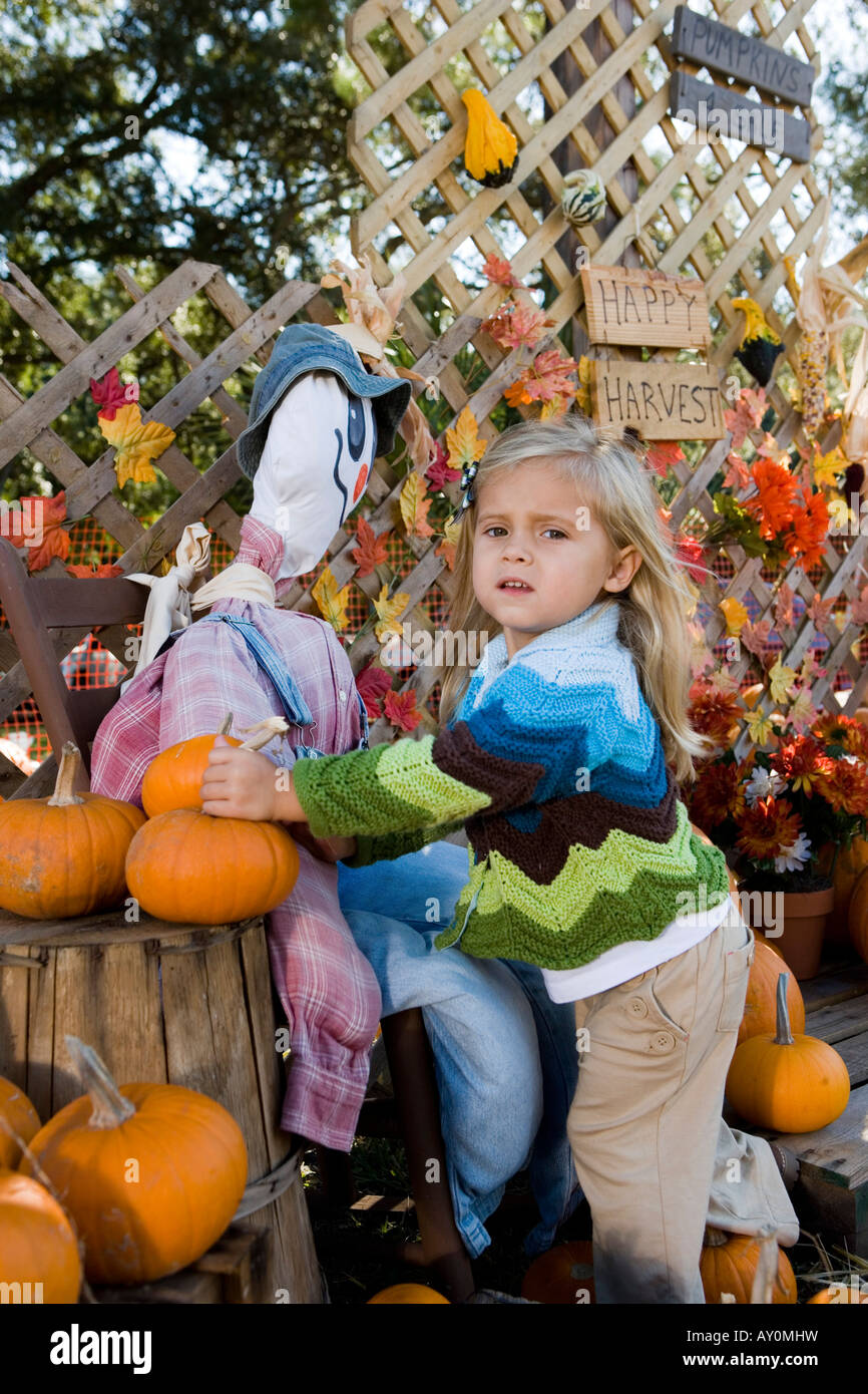 Portrait Of A Cute Girl In Warm Clothing Standing By Scarecrow Stock