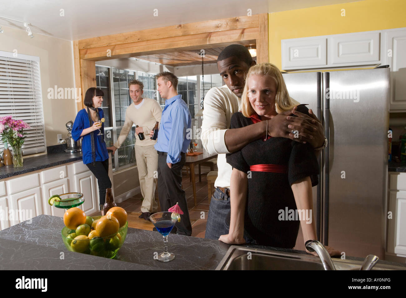Portrait of man embracing woman in domestic kitchen while their friends ...