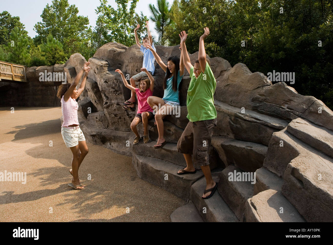Teenagers with their arms raised sitting on rocks and playing Stock ...