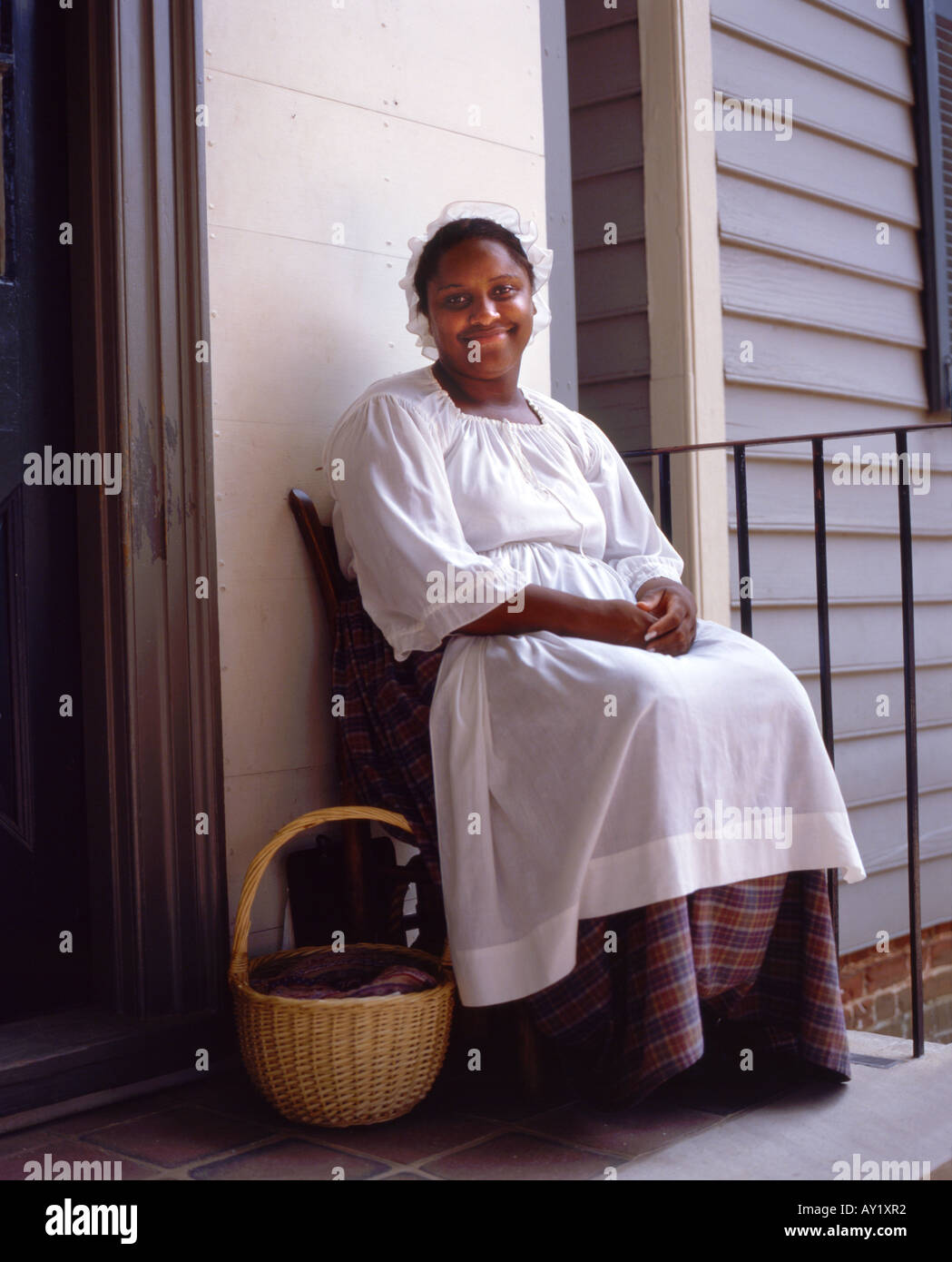 A black woman sitting on the porch of a house in Colonial Williamsburg ...
