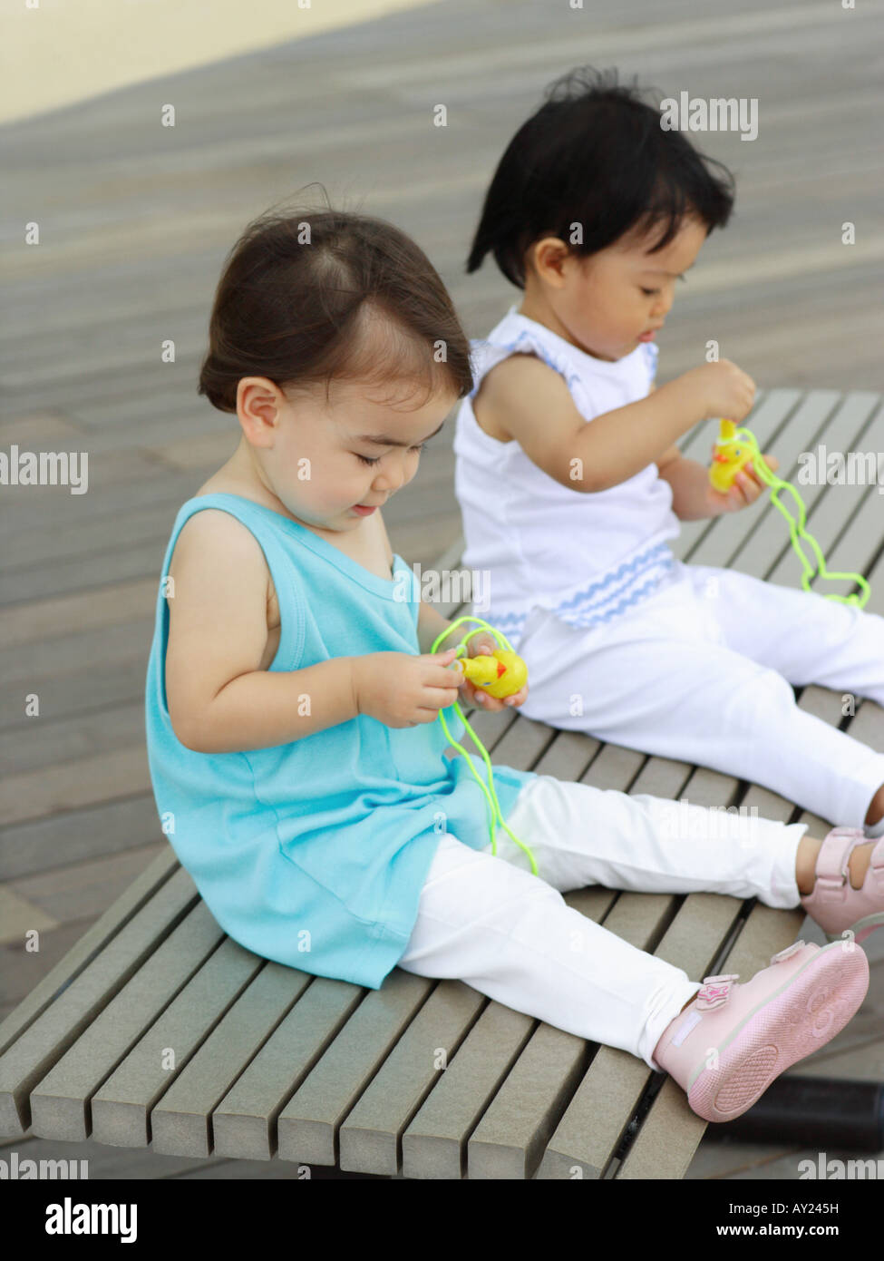 Two baby girls sitting on a bench and playing with toys Stock Photo - Alamy
