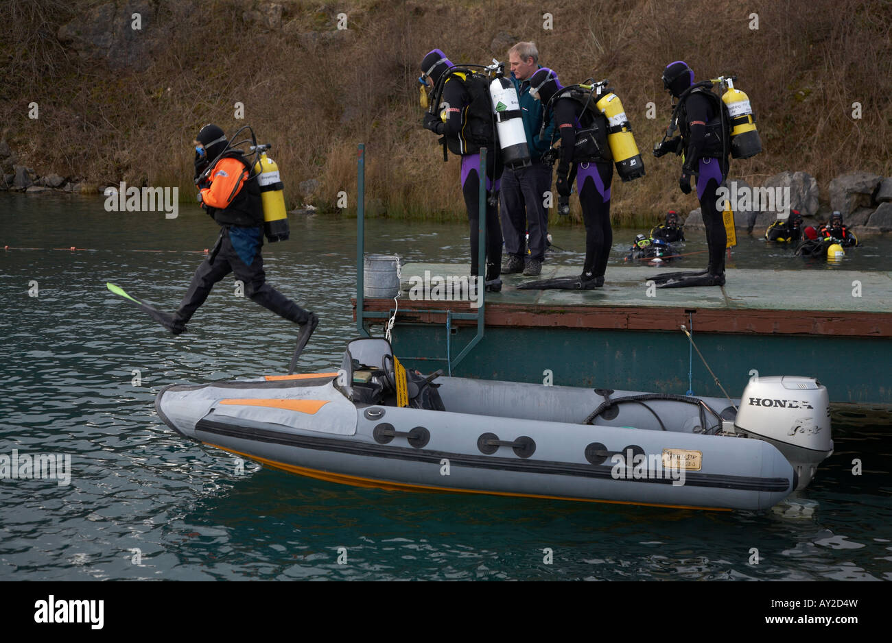 scuba diver jumping into water with other divers waiting on the jetty next to a speed boat Stock
