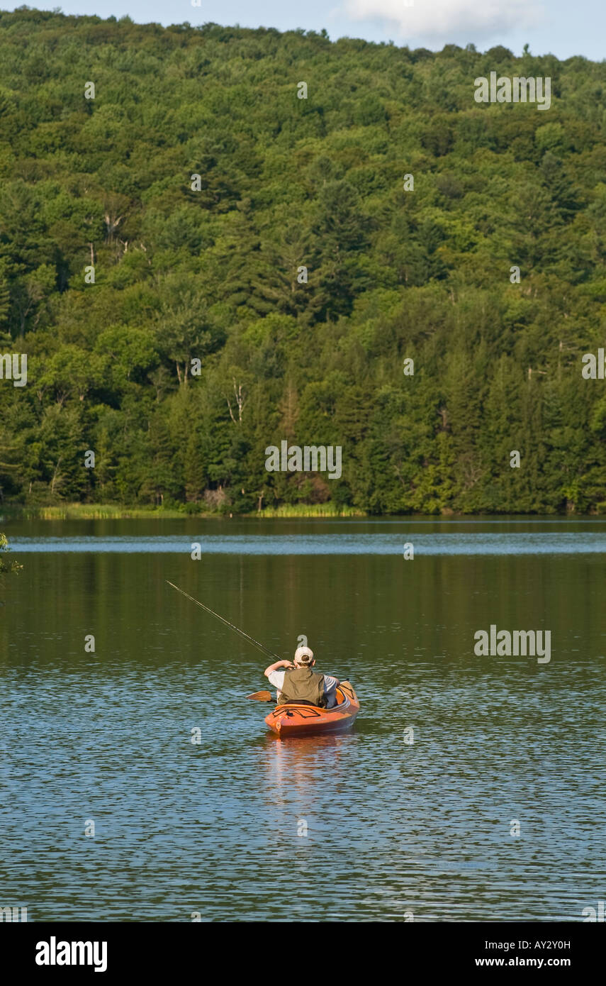 A lone teenage boy wearing a fishing vest and a hat fishing from