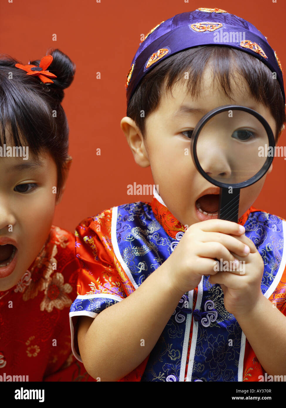 Close-up of a boy looking through a magnifying glass with his sister beside him Stock Photo