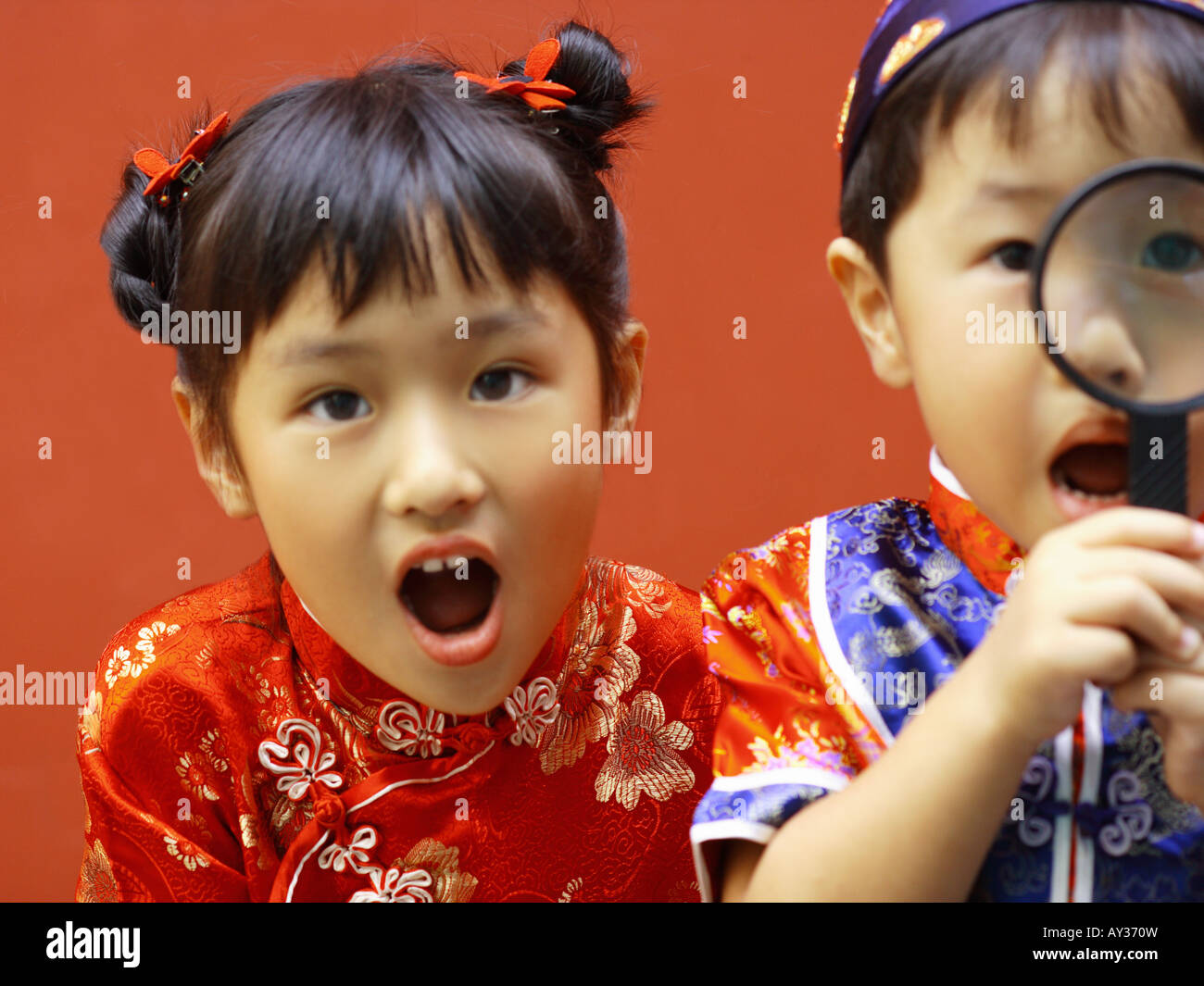 Close-up of a boy looking through a magnifying glass with his sister beside him Stock Photo