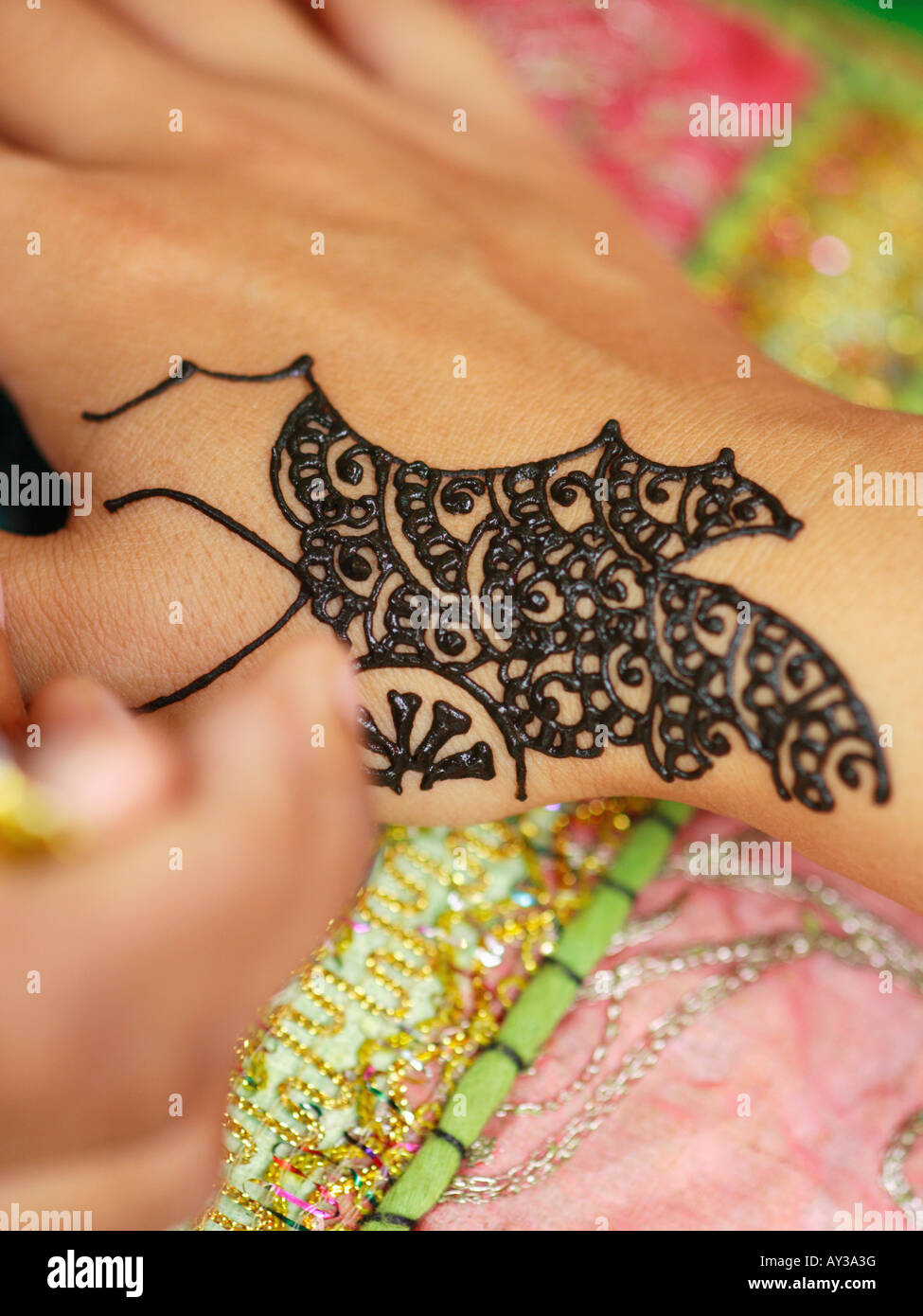 Closeup of a woman's hand applying henna tattoo on another woman's