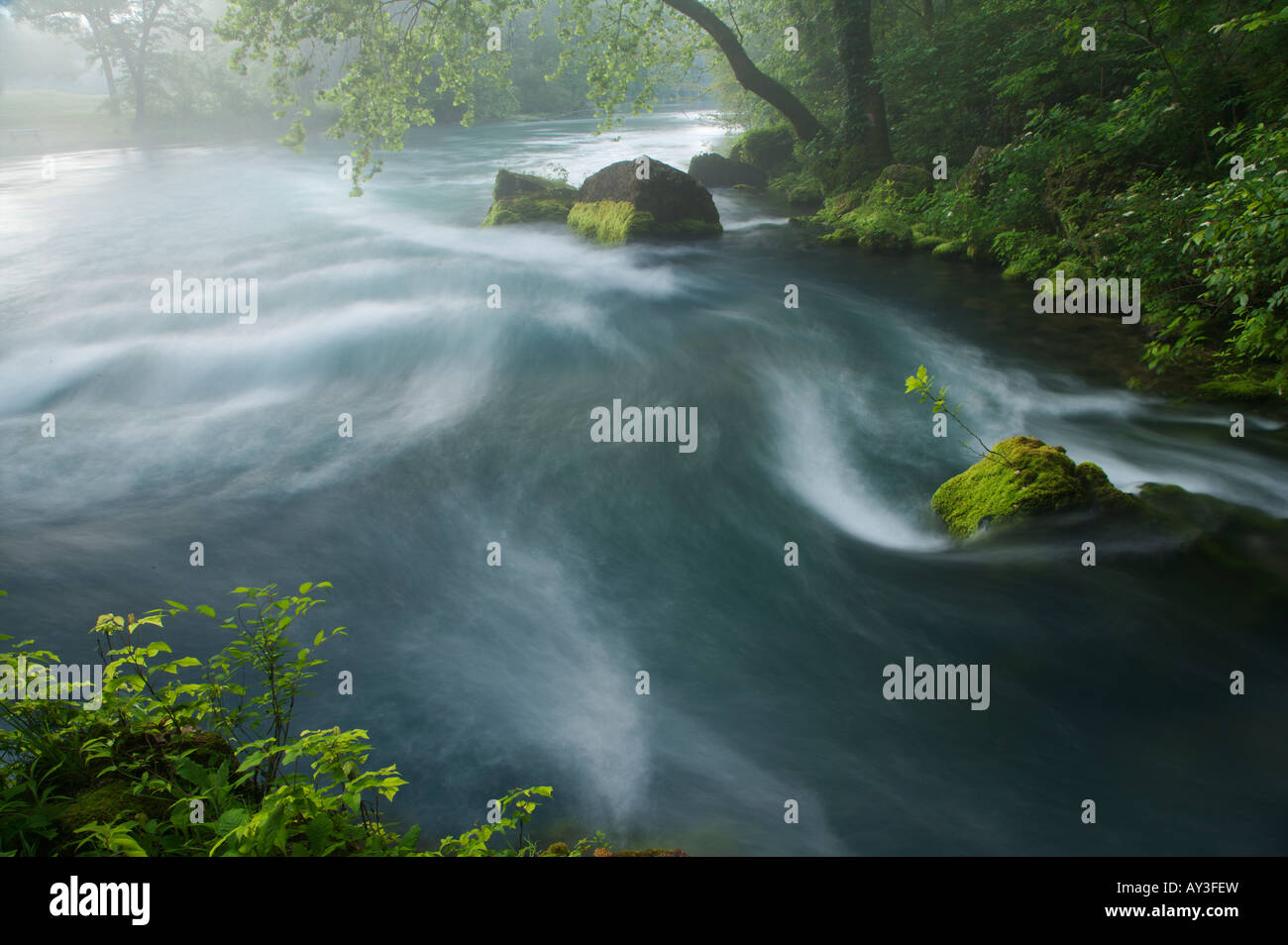 Water flowing from underground spring in early morning with fog rising from water Stock Photo