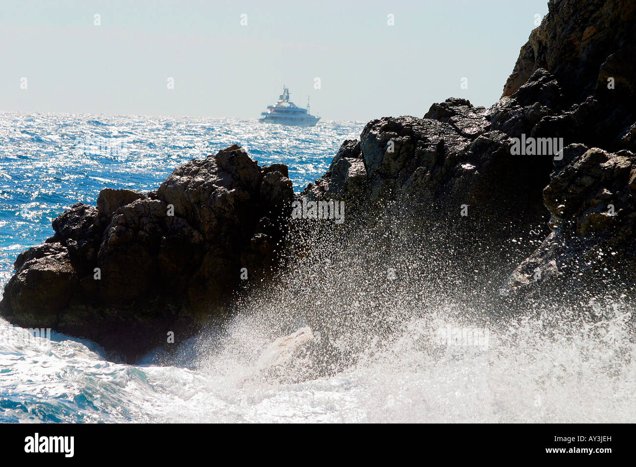 Waves crashing on rocks by shore, ship in background. Stock Photo