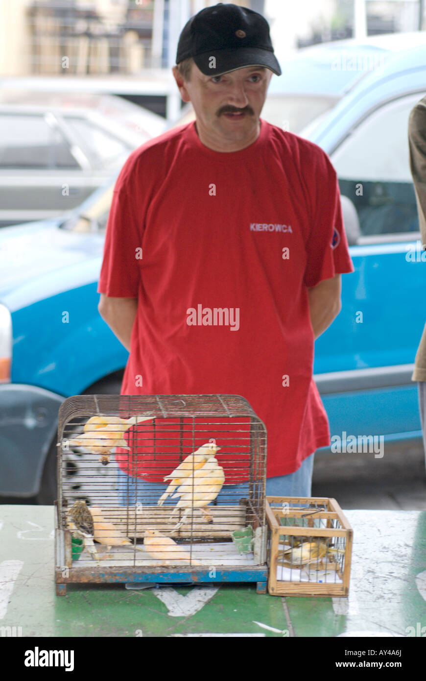 A man in a red tee shirt with a cage full of canaries for sale at a street market in Krakow Poland Stock Photo
