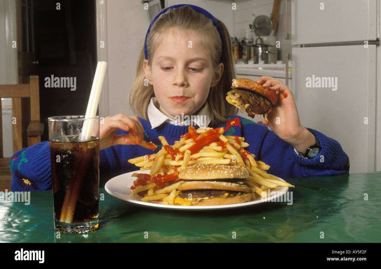 Young teenage schoolgirl eating unhealthy fast food, a huge hamburger and chips drinking coke at home in after school London HOMER SYKES Stock Photo