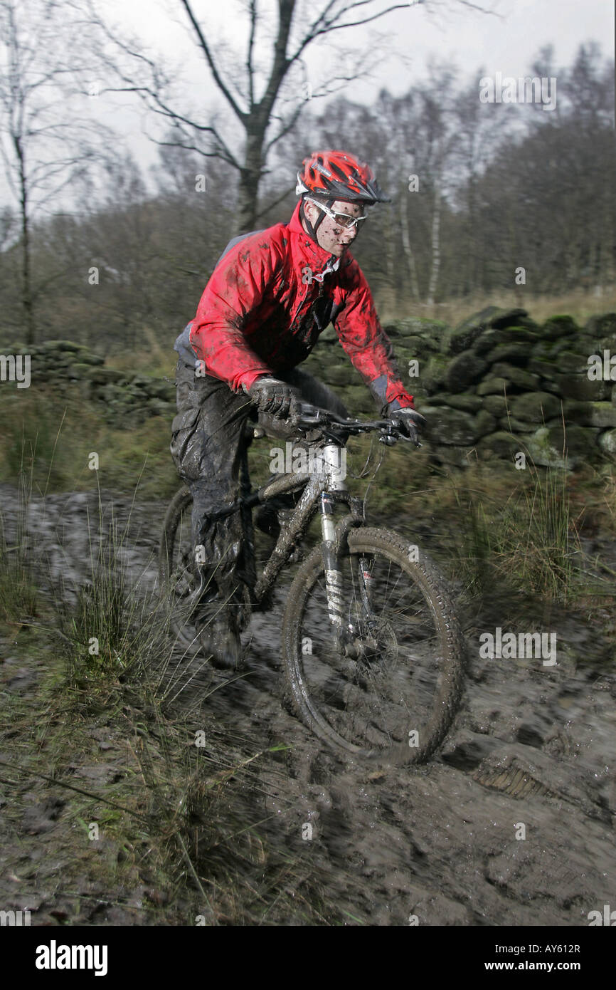 A mountain biker covered in mud rides his bike along a muddy track