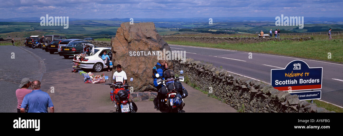 Crossing the Border from England to Scotland at Scottish Borders by road sign with few people, cars, motorbikes and distant hill Stock Photo