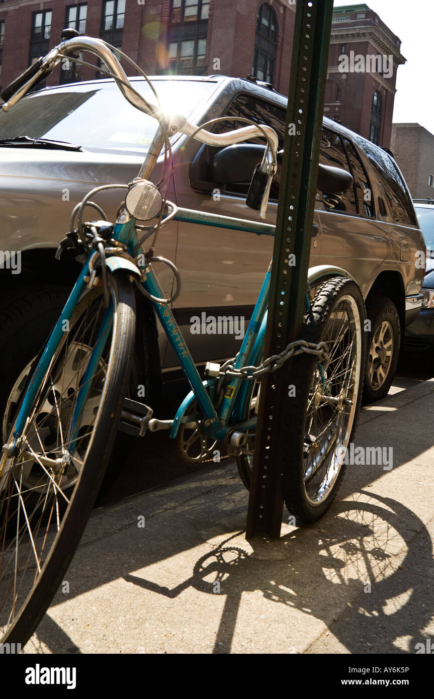 Bicycle chained to signpost beside parked SUV Stock Photo