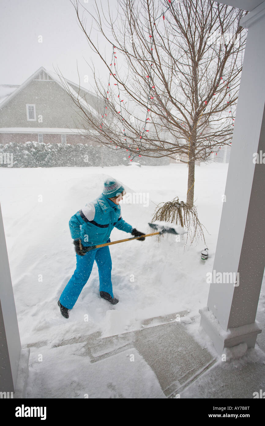 Shovelling Snow A woman in a blue snow suit lifts snow onto a growing snowbank A storm obscures the next house Stock Photo