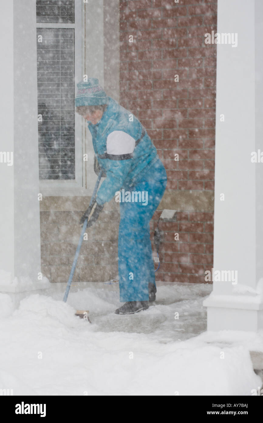 Clearing Snow in Ottawa A woman in a blue snow suit brushes snow off a porch Stock Photo