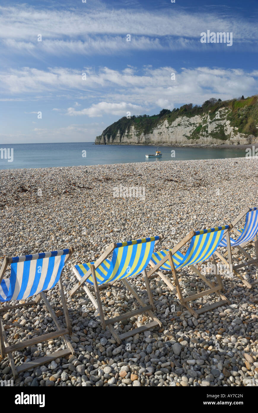 View of Beer beach in Devon, UK, with blue deckchairs in the foreground and a small boat in the sea Stock Photo