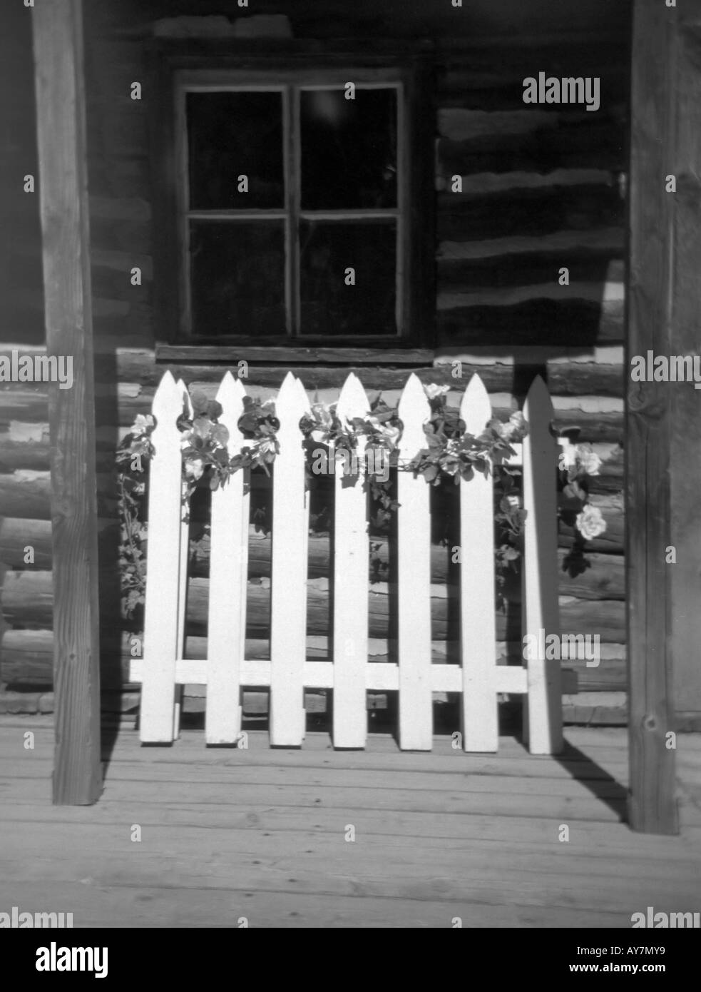 A White Picket Fence Stands In Front Of An Old Log Cabin In Stock