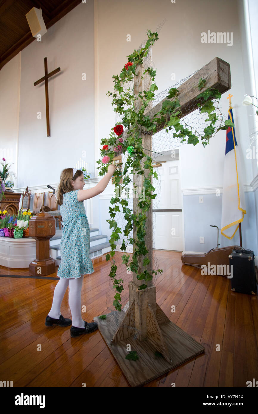 A young girl places a flower on a large cross in a church during Easter Mass in Connecticut USA Stock Photo