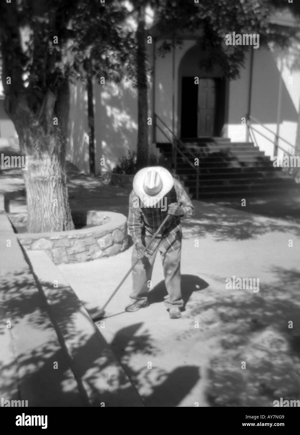 A reverent and elderly Hispanic man sweeps the courtyard of the Chapilla de San  Lorenzo, in San Lorenzo, New Mexico. Stock Photo