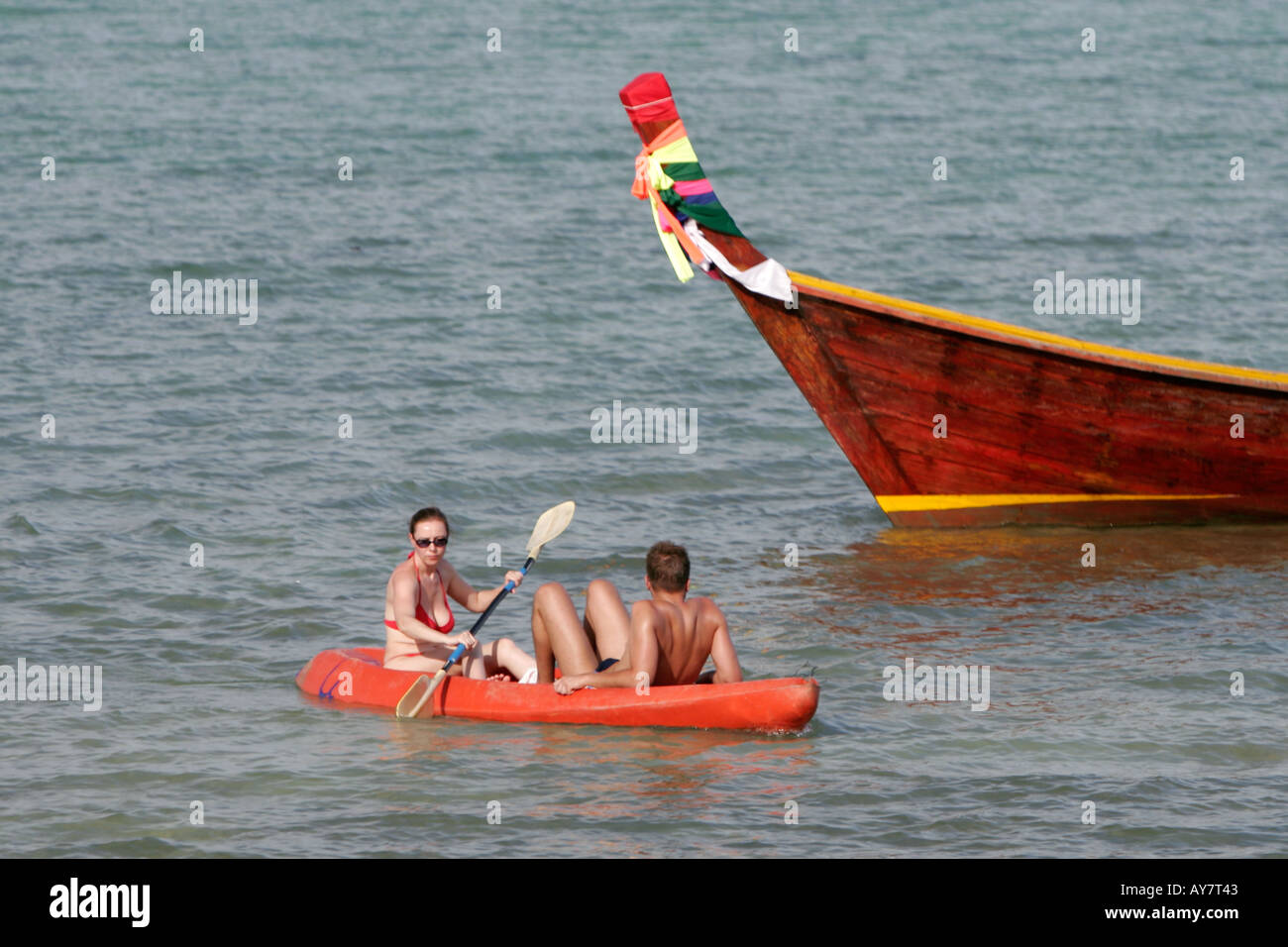 Couple in sea kayak paddle past longtail boat Ko Ngai island Thailand