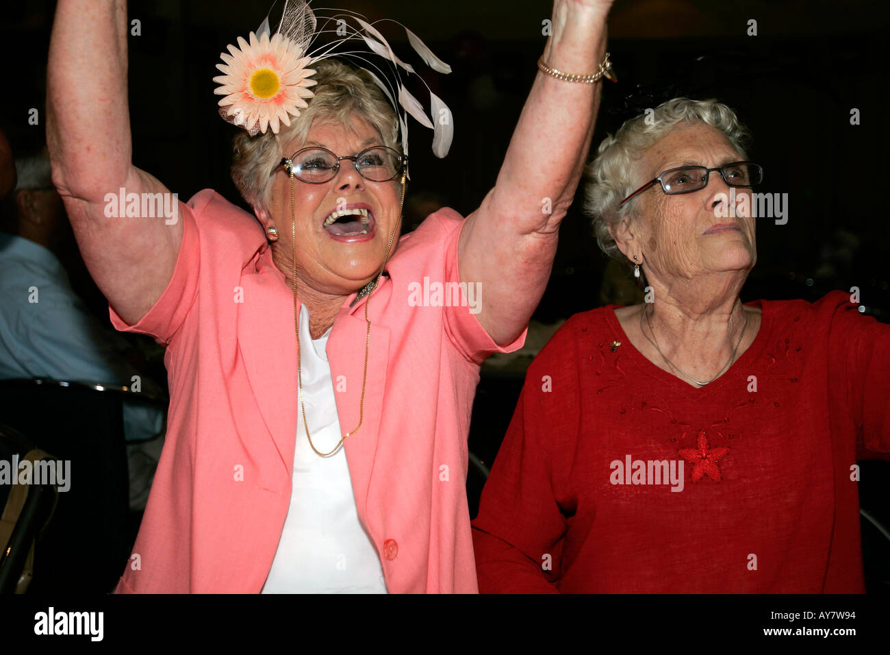 Older woman in Melbourne Cup outfit and hat cheers watching her winning horse on television Australia Stock Photo