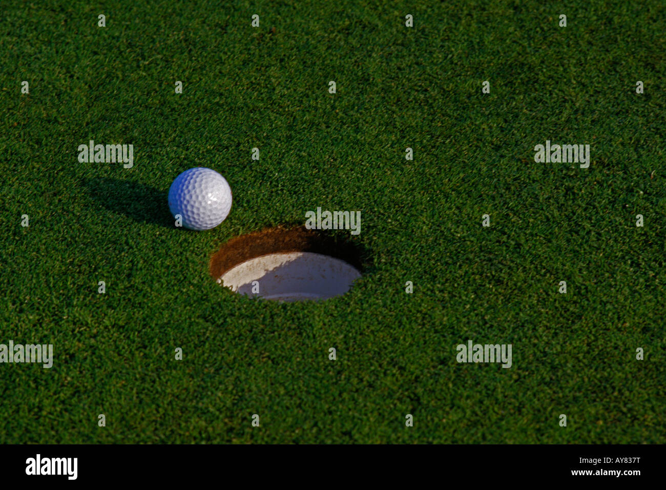 Golf ball sitting near the hole Stock Photo