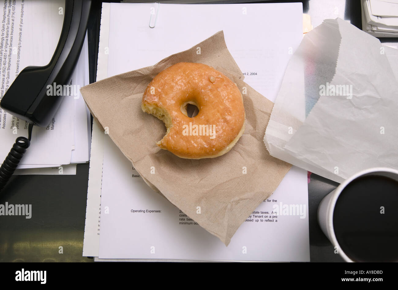 Office desk of busy office worker with phone off hook and a bite out of donut Stock Photo