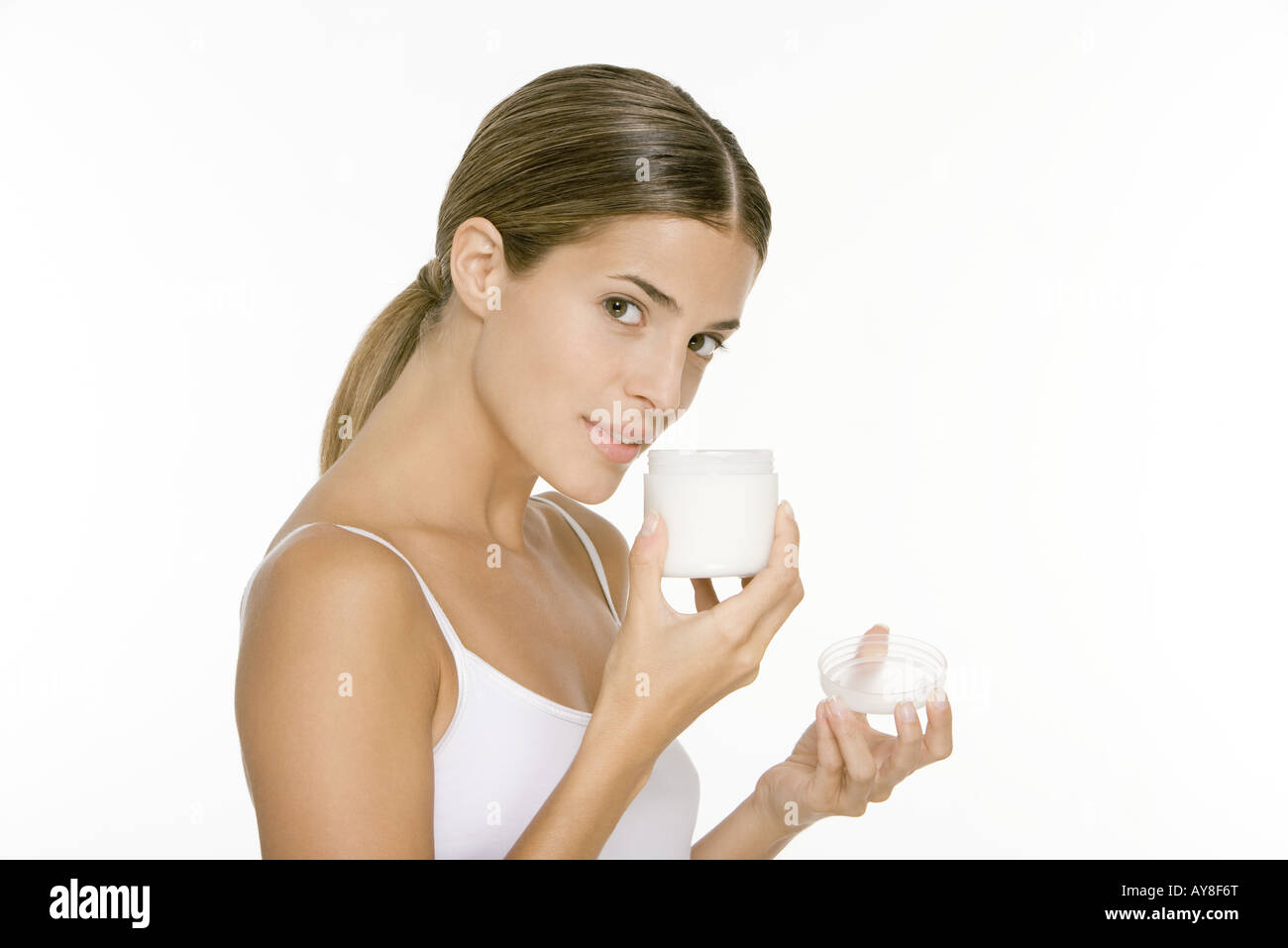 Woman smelling jar of moisturizer, looking at camera Stock Photo