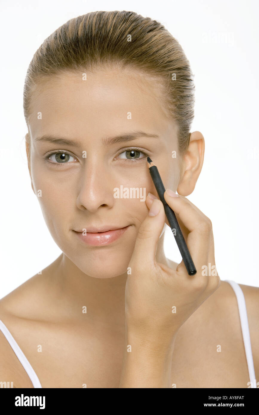 Woman applying eyeliner, smiling at camera, close-up Stock Photo