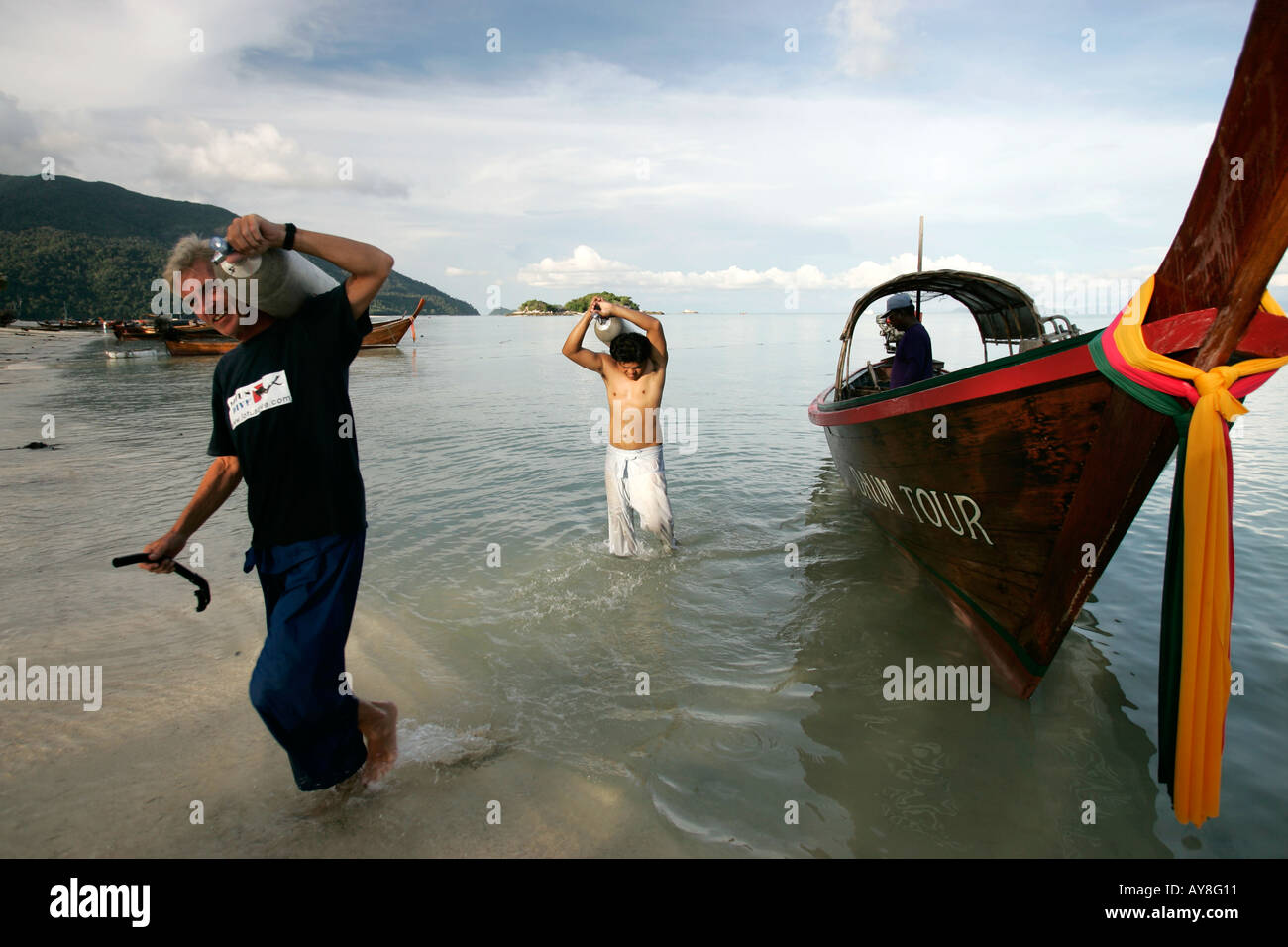 Two men carry diving tanks ashore from traditional longtail boat Ko Lipe island Thailand Stock Photo
