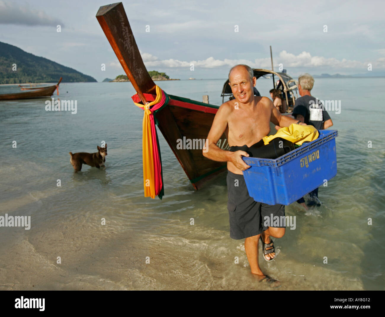 Man carries ashore diving equipment from traditional longtail boat Ko Lipe island Thailand Stock Photo