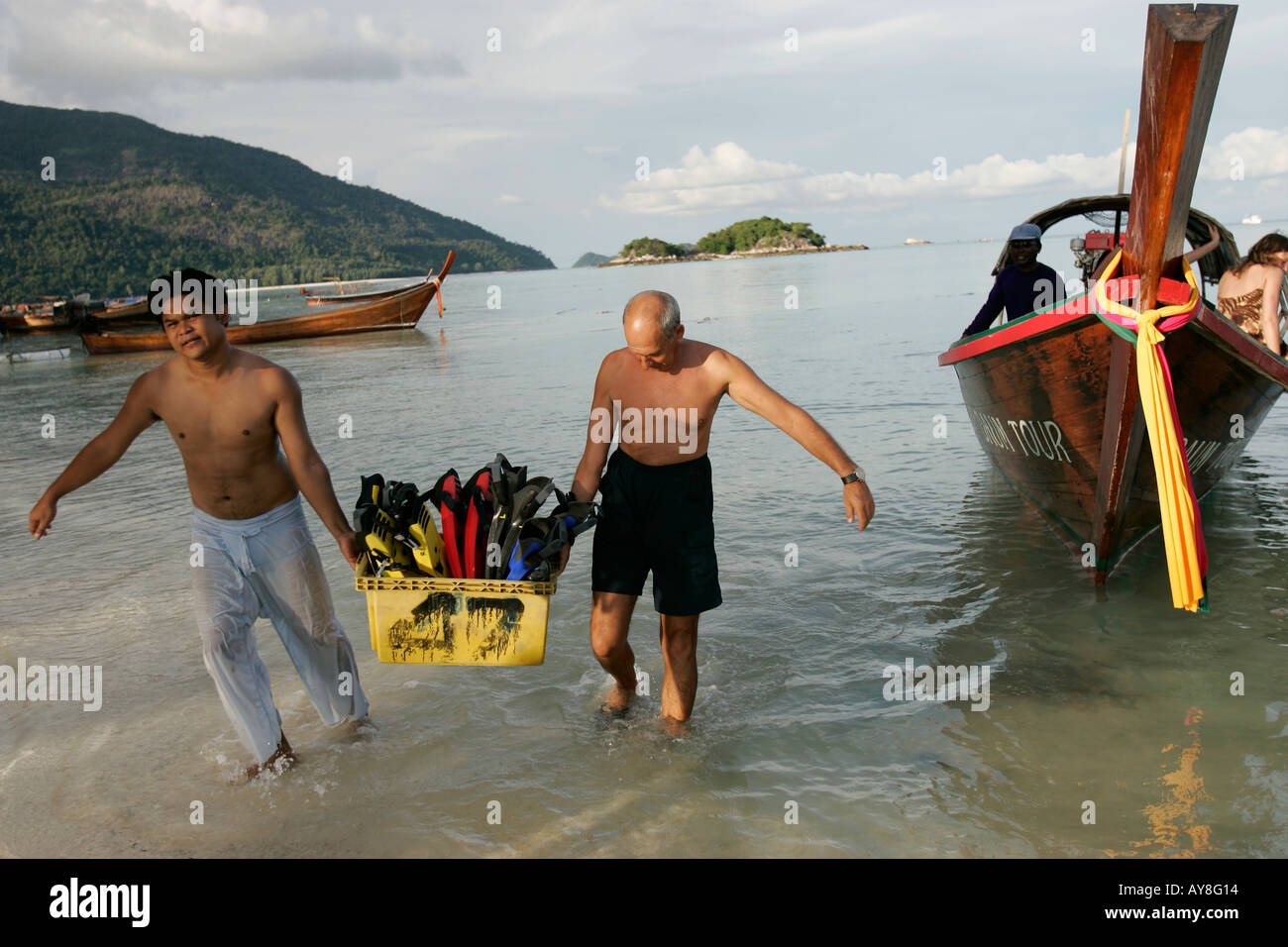 Men carry ashore diving equipment from traditional longtail boat Ko Lipe island Thailand Stock Photo