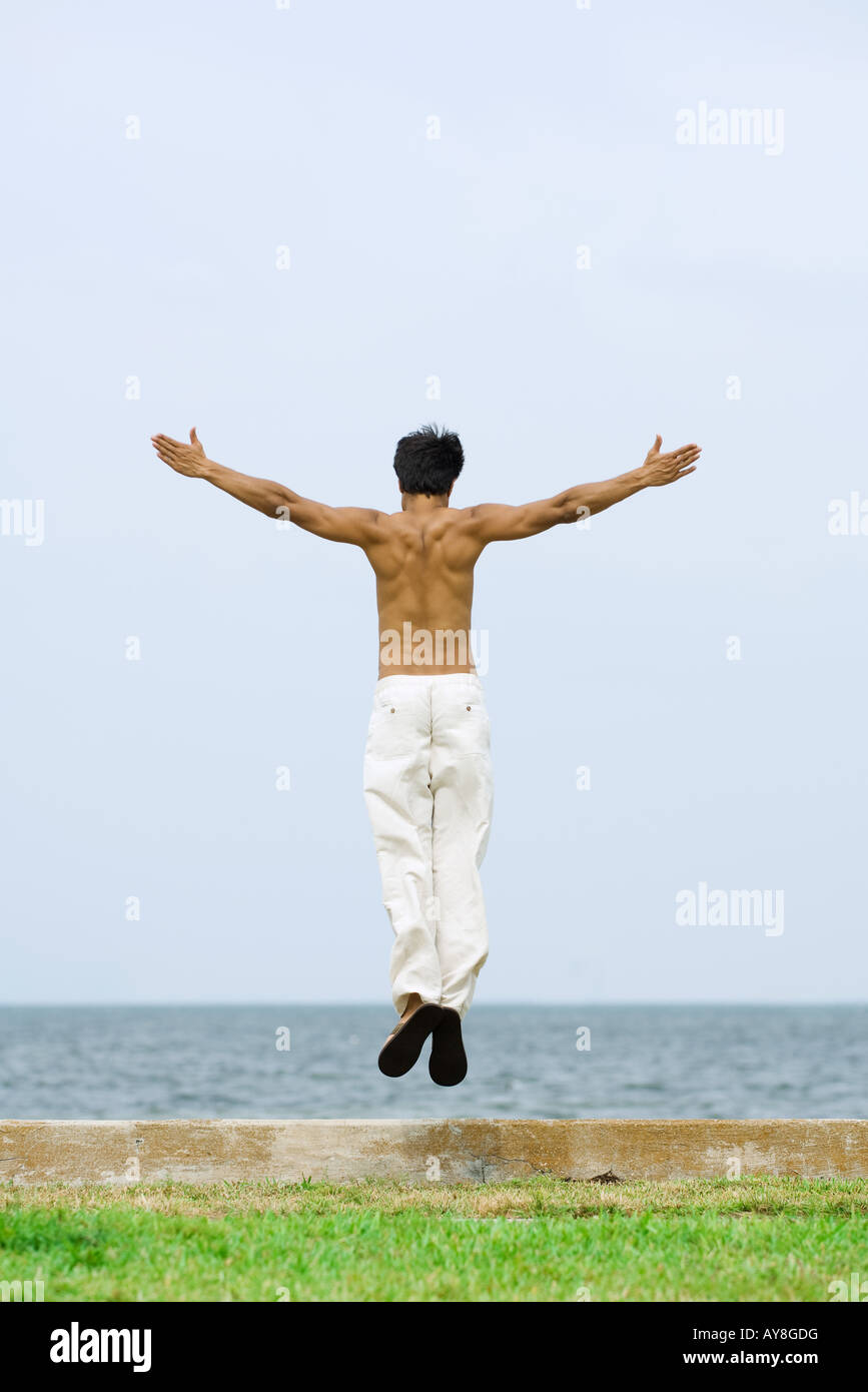 Man jumping in the air at the beach, arms outstretched, rear view Stock Photo