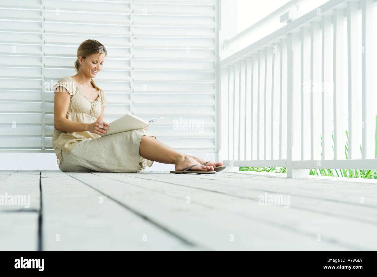 Woman sitting on porch reading book, low angle view Stock Photo