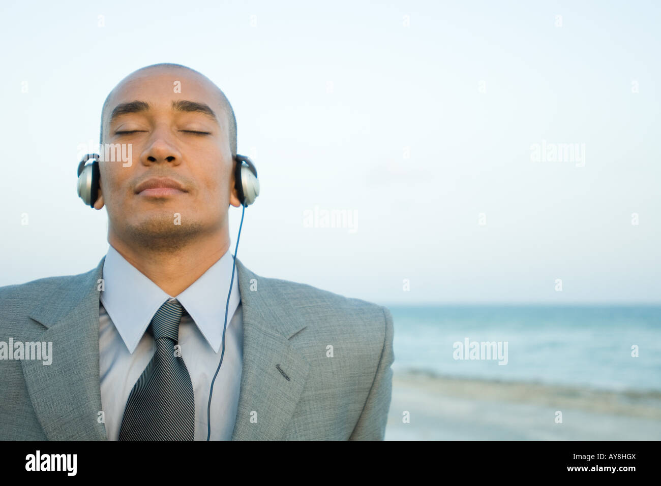 Businessman listening to headphones at the beach, eyes closed, close-up Stock Photo