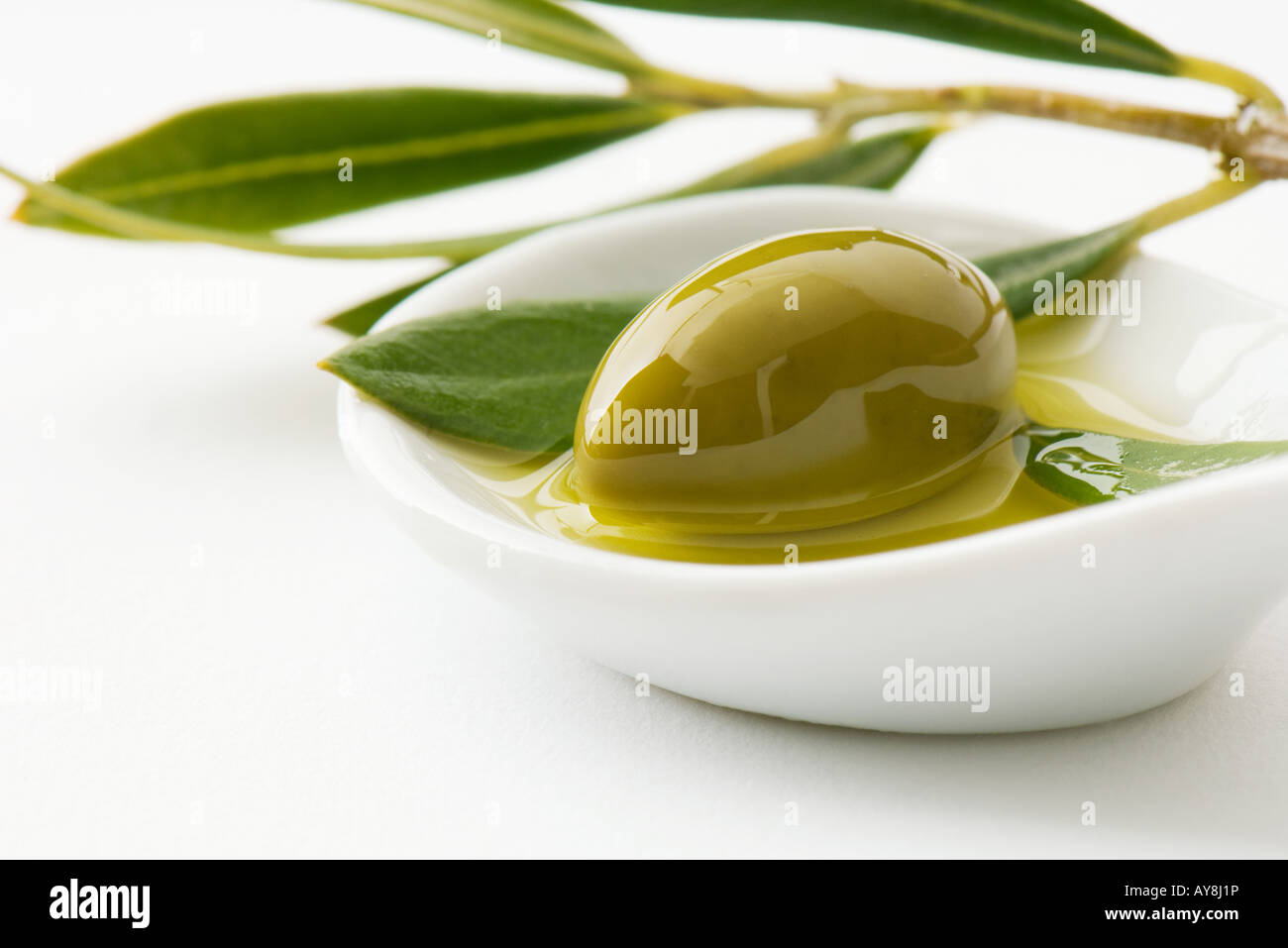 Green olive and sprig of leaves in small dish of olive oil, closeup
