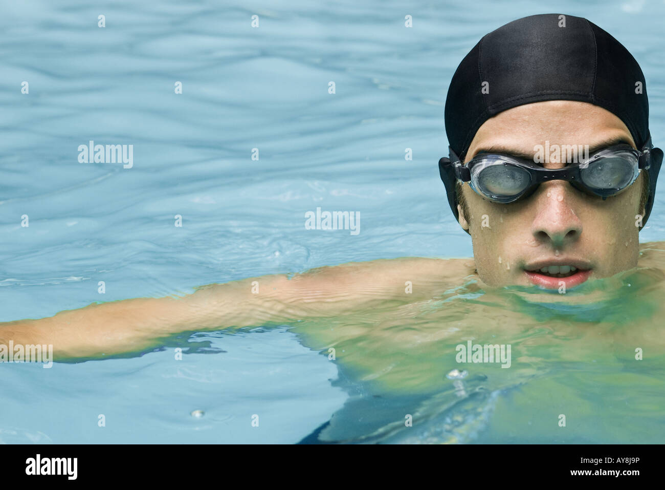 Man in swimming pool wearing goggles and bathing cap, looking at camera, closeup Stock Photo